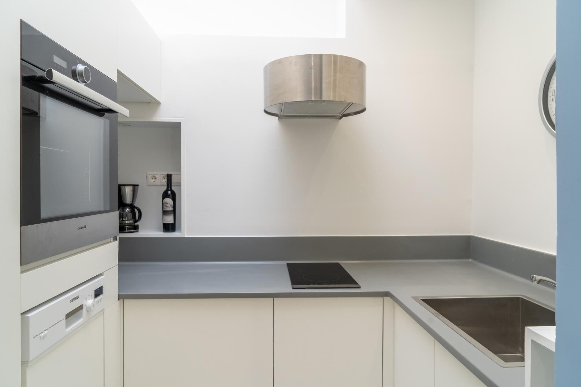 Een moderne keuken met een inbouwoven, een koffieapparaat en een fles wijn op het aanrecht.