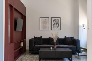 A living room with a dark-colored sofa, a coffee table with a candle, and two framed artworks on the wall.