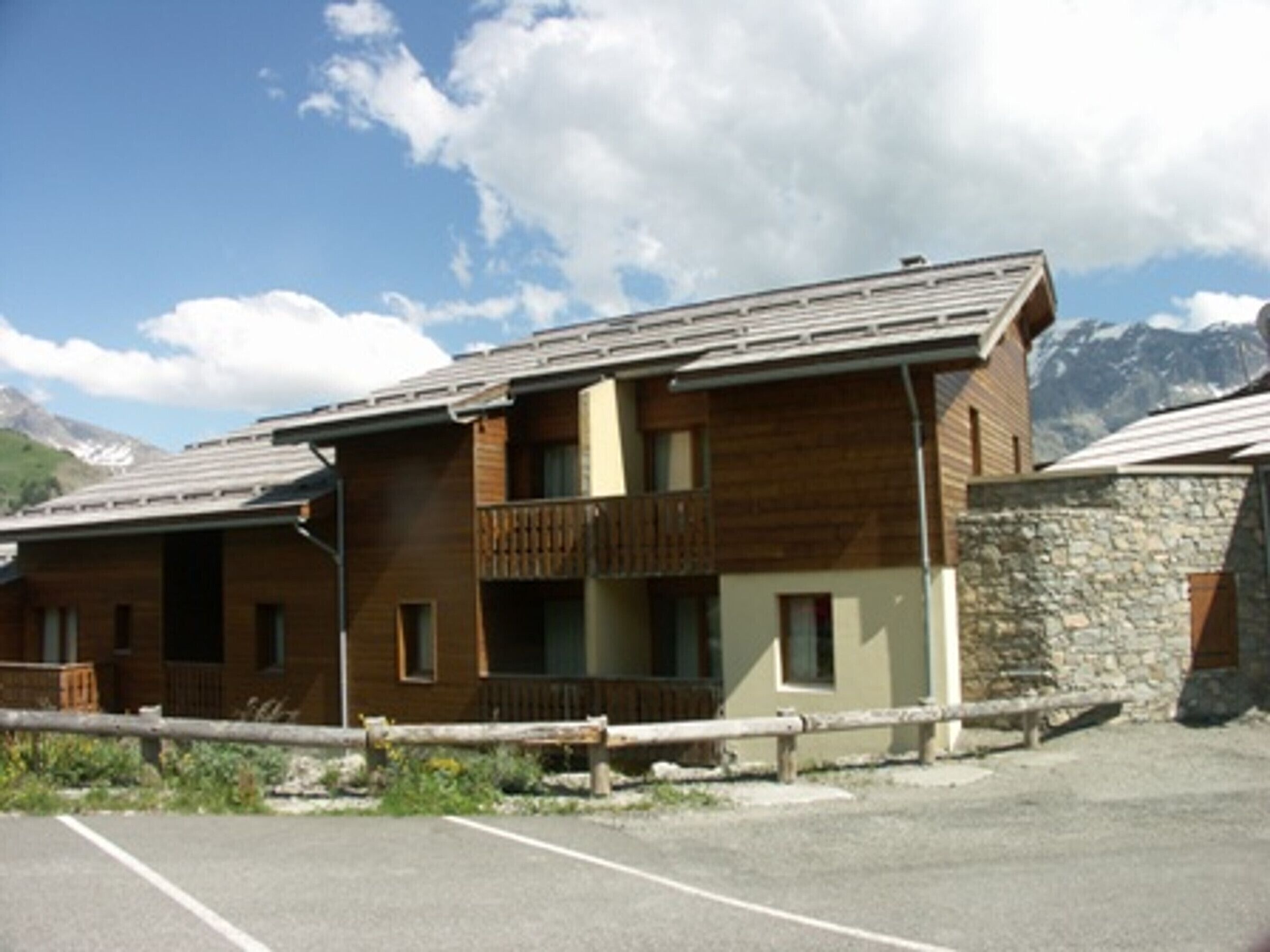 Un bâtiment en bois à deux étages, doté d’un balcon, d’un mur en pierre et d’un parking.