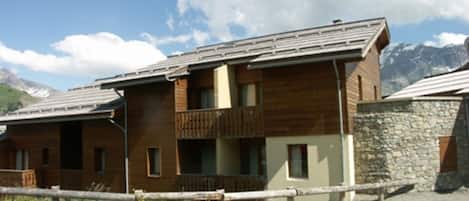 A two-story wooden building with a balcony, a stone wall, and a parking lot.