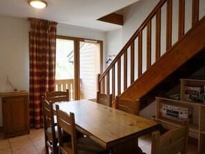 A dining area with a wooden table and chairs, a staircase, and a view of the outside. - Duplex near slopes - 7 guests (Orcières Merlette)