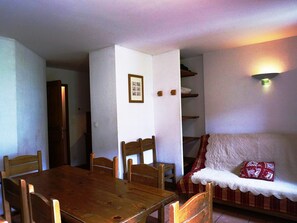 A dining area with a wooden table and chairs, a white cushioned bench, and a framed picture on the wall. - Duplex near slopes - 7 guests (Orcières Merlette)