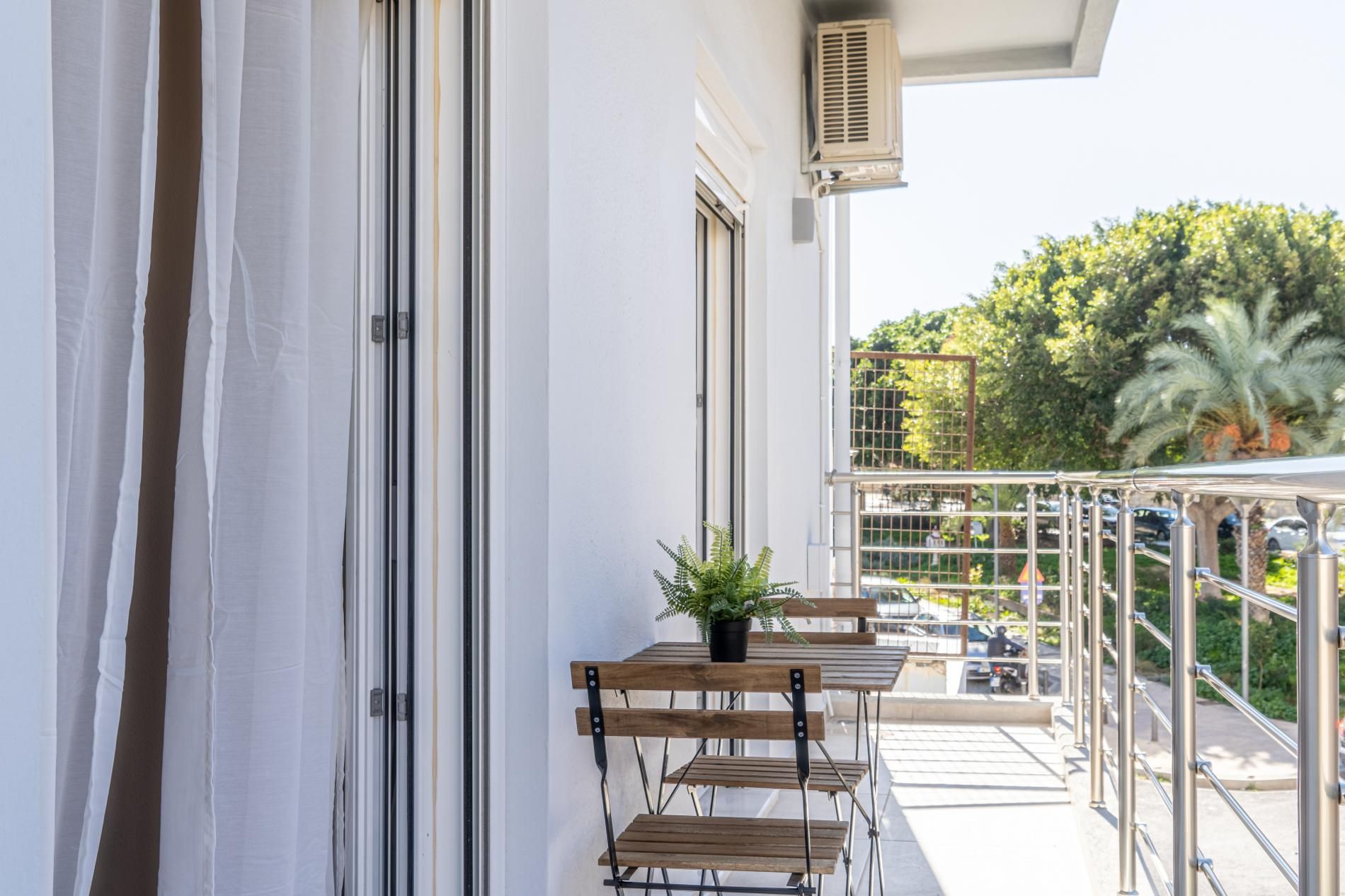 A balcony with a potted plant, a table, and chairs.