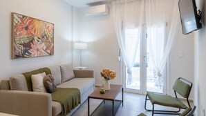 Una sala moderna con un sofá, una mesa de centro, una silla, un cuadro y un televisor montado en la pared.