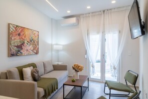 A modern living room with a sofa, a coffee table, a chair, a painting, and a TV mounted on the wall. - Pananos Sq. House I (Heraklion)