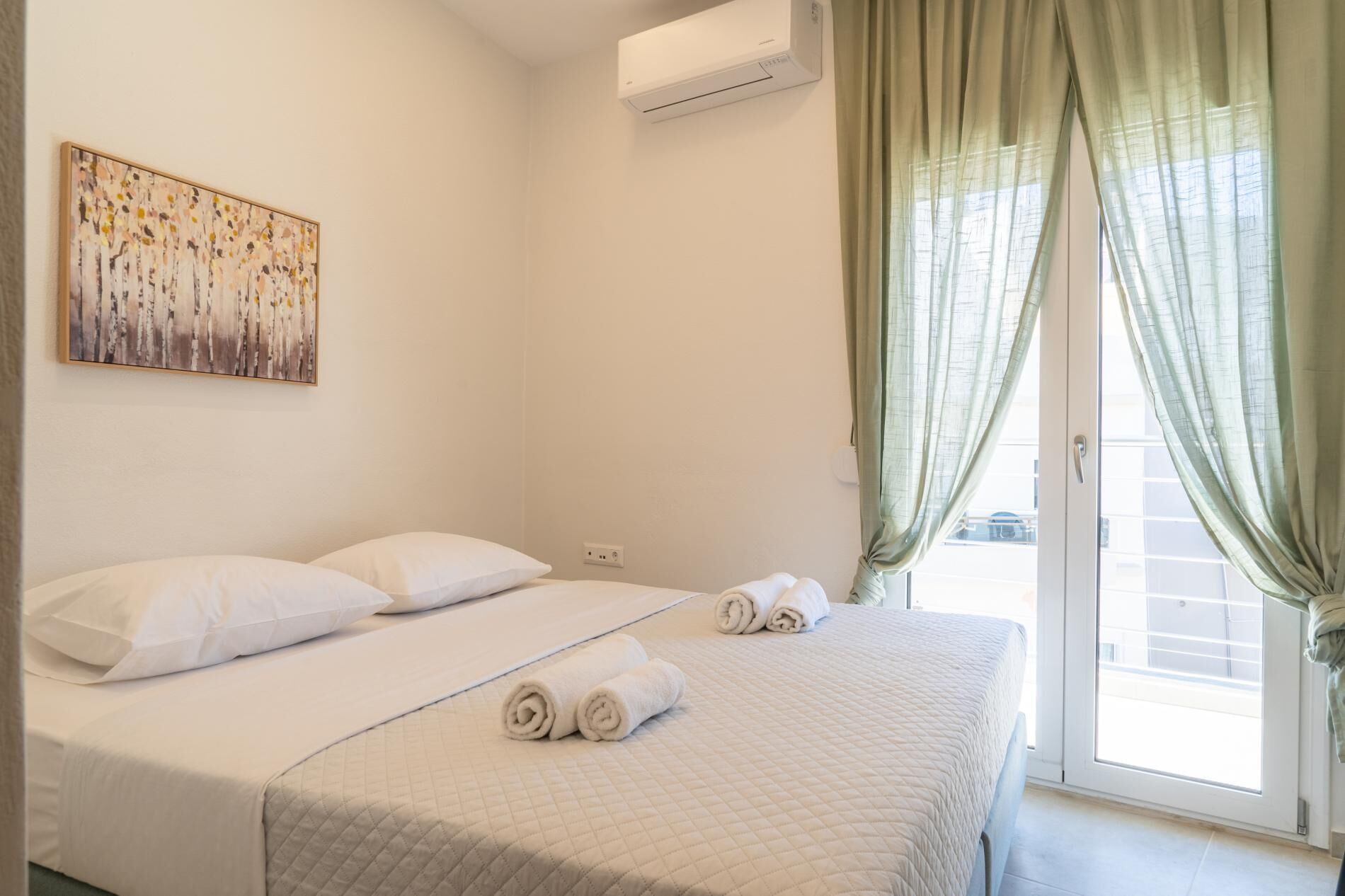 Habitación de hotel con cama, un cuadro, aire acondicionado y vistas a través de una ventana con cortinas.