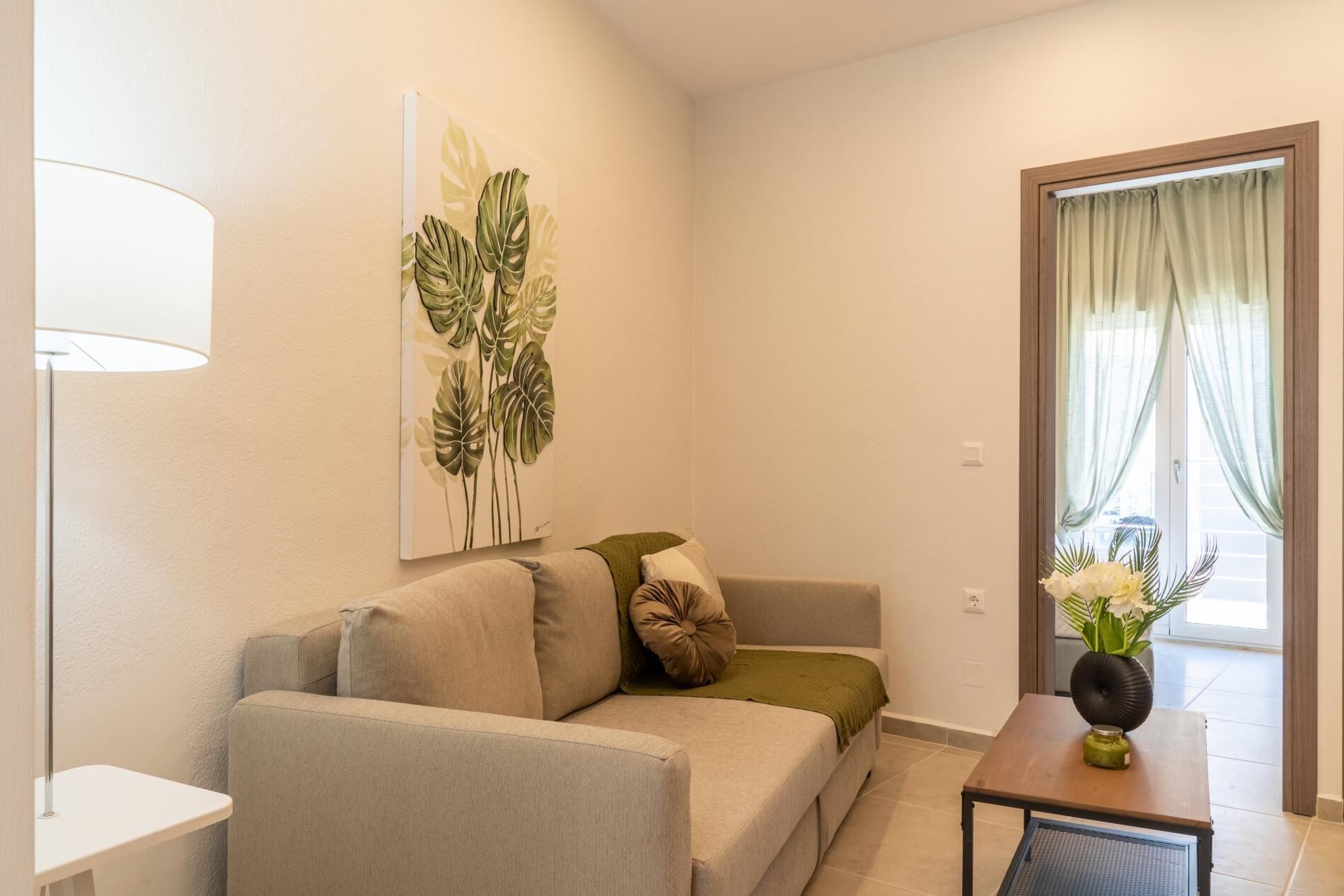A modern living room with a sofa, a small table, and a painting of leaves on the wall.