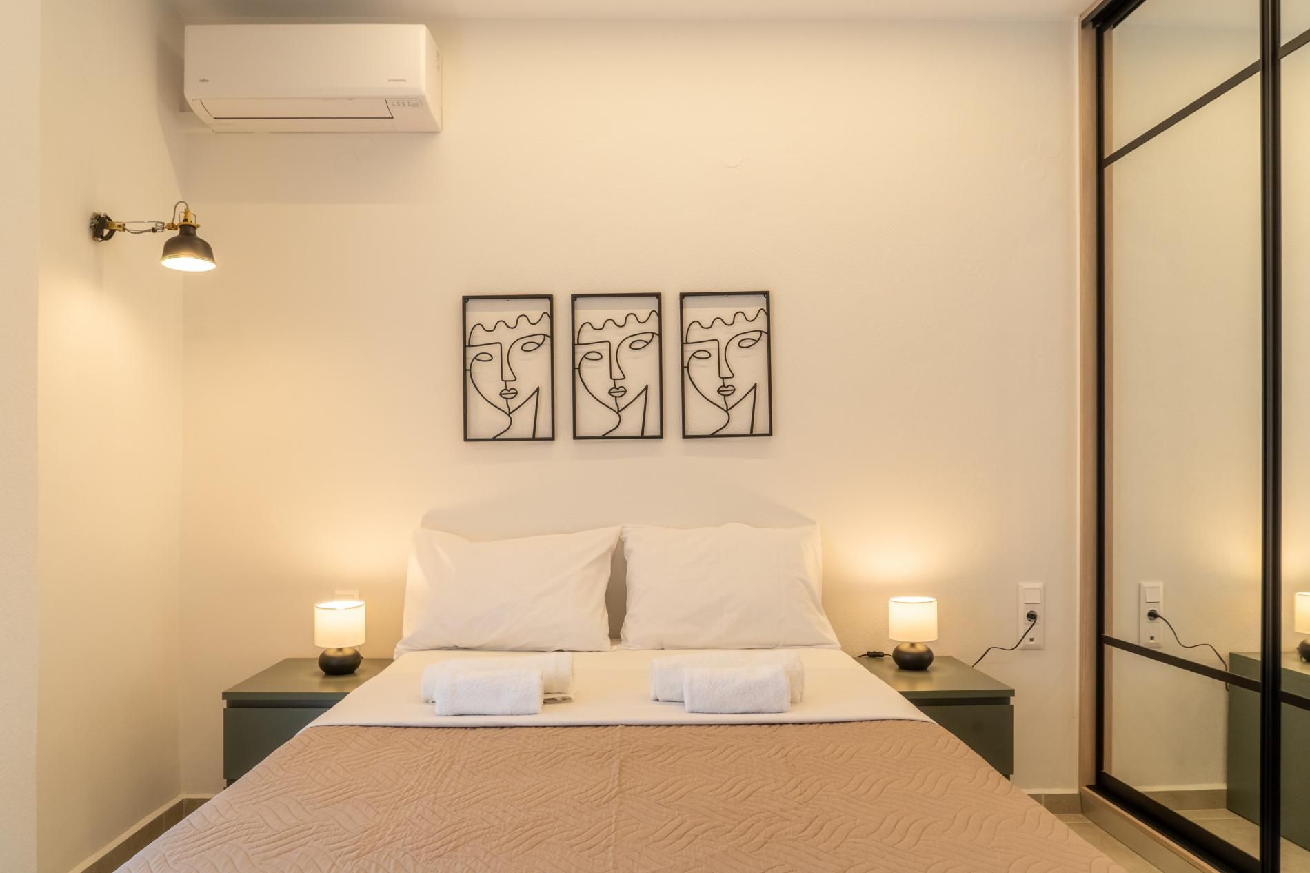 A hotel room with a bed, two bedside lamps, and three abstract wall art pieces.