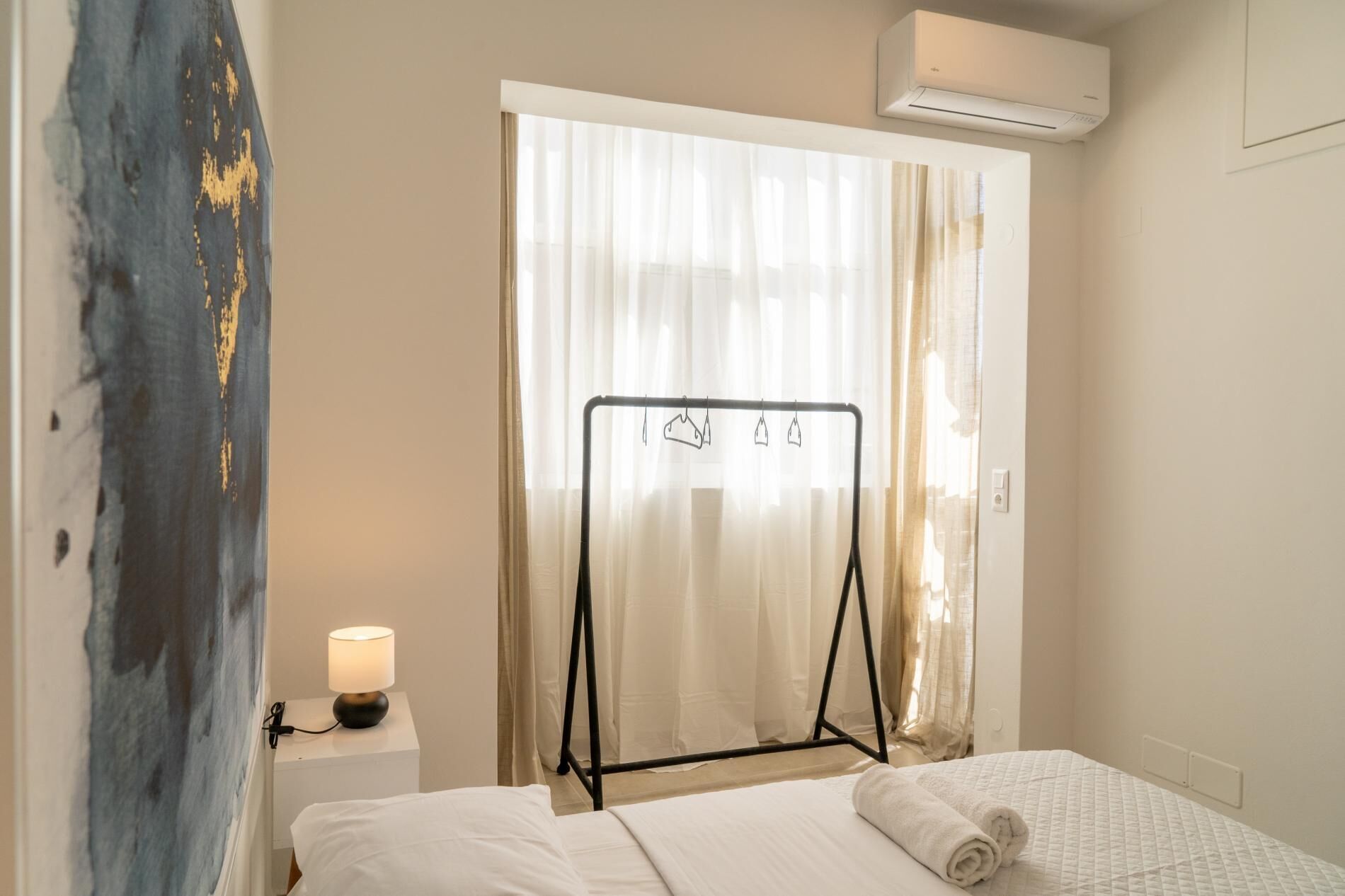 Une chambre d’hôtel comprenant un lit, un climatiseur fixé au mur, une table de chevet avec une lampe et un porte-vêtements.