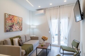 Ein modernes Wohnzimmer mit einer Couch, einem Couchtisch, einem Sessel, einem Gemälde und einem an der Wand befestigten Fernseher.