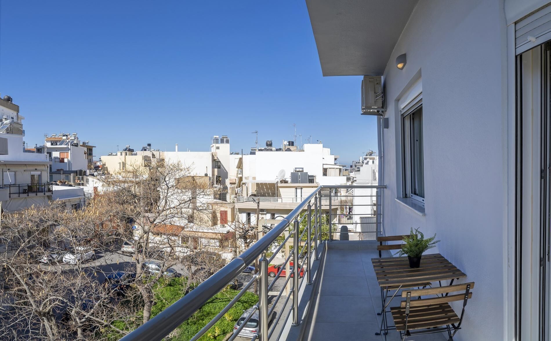 Un balcon donnant sur un paysage urbain, une petite table avec une plante et une rambarde.