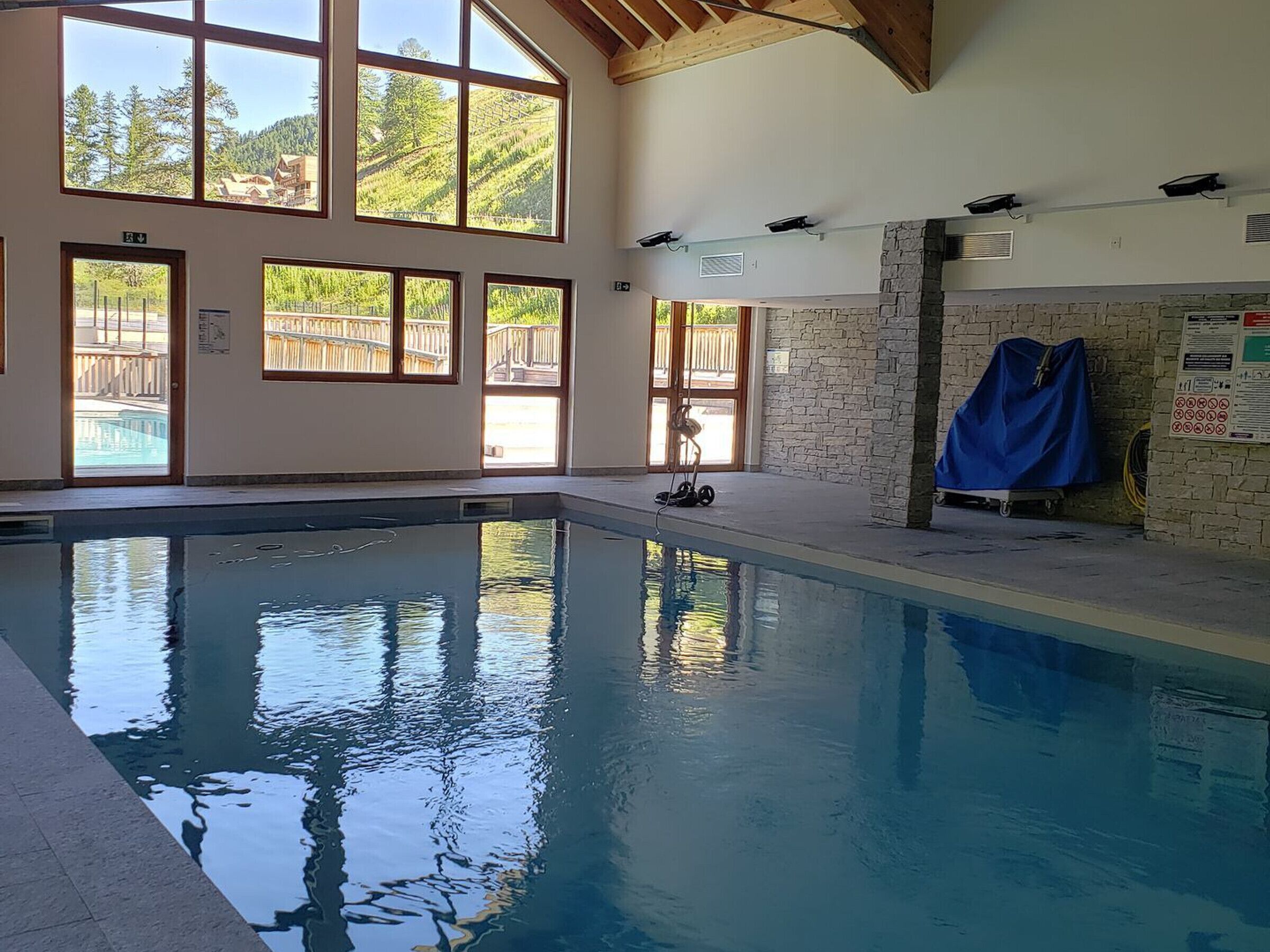 A swimming pool with clear water, large windows, and a stone wall.