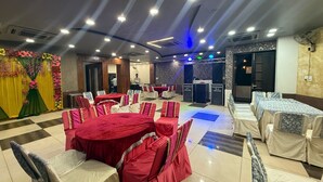 A banquet hall with round tables covered in red tablecloths, white chairs, and a stage with speakers.