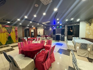 A banquet hall with round tables covered in red tablecloths, white chairs, and a stage with speakers. - Hotel M9 (Ludhiana)