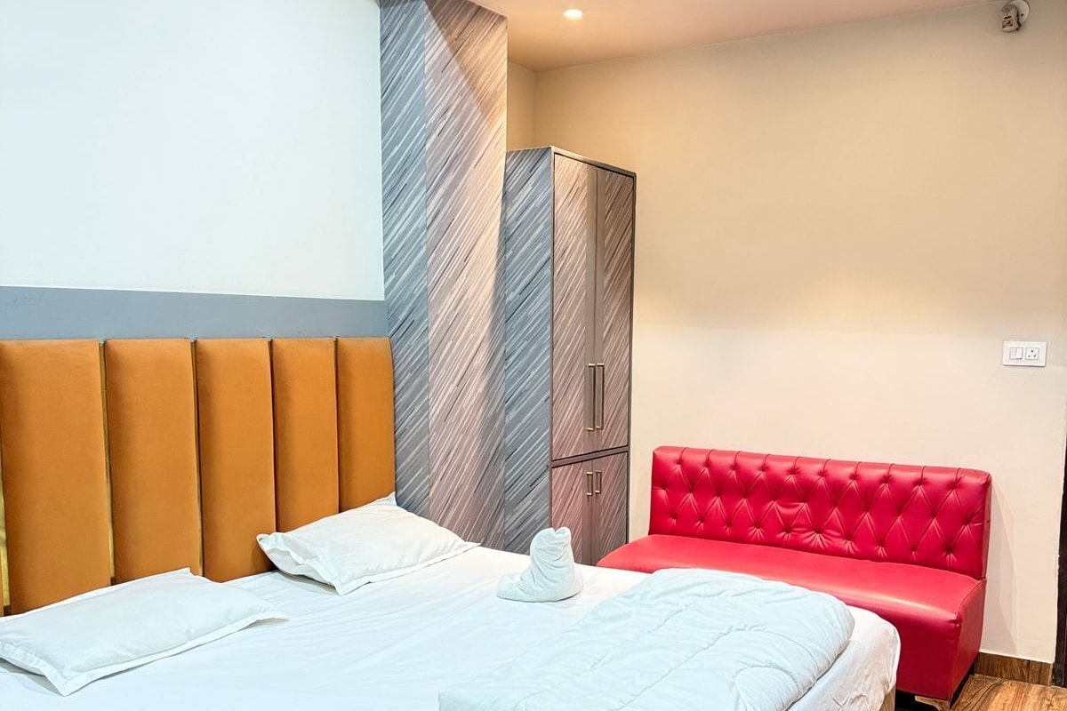 A modern hotel room with a large bed, a red upholstered bench, and a wardrobe.