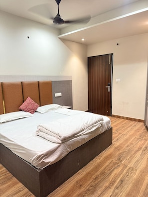 A bedroom with a bed, a ceiling fan, a wooden floor, and a door. - Hotel M9 (Ludhiana)