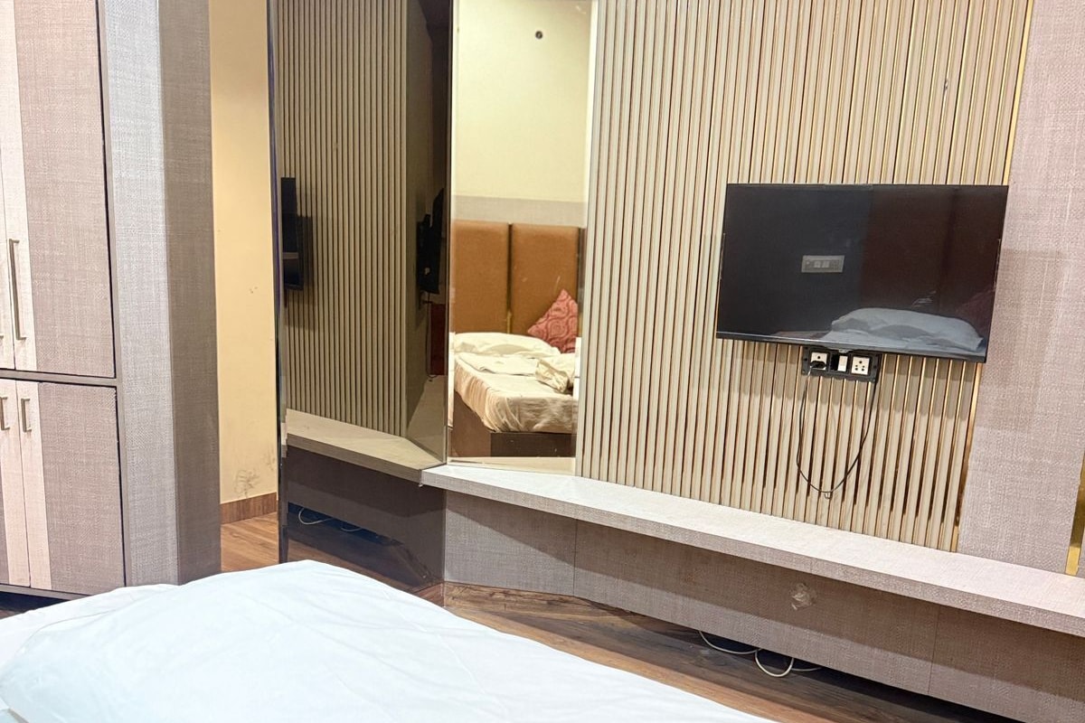 A hotel room with a bed, a mirror, a television, and a wardrobe.