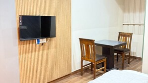 A hotel room with a bed, a desk with a chair, a television mounted on a wooden panel, and a window with curtains.