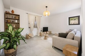 Ein Wohnzimmer mit einer Couch, einem Fernseher, einer Pflanze und einer Pendelleuchte.