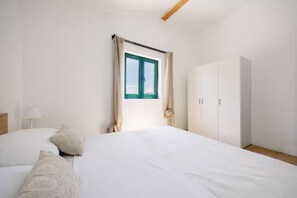 Ein Schlafzimmer mit Bett, einem Fenster mit Vorhängen, einem Kleiderschrank und einer Lampe.