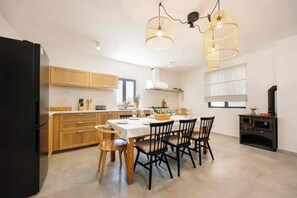 A modern kitchen with wooden cabinets, a dining table set for four, and a black oven. - Villa Jadra (Kornati)