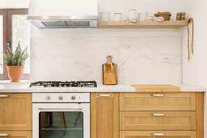 A modern kitchen with a gas stove, oven, wooden cabinets, and a marble backsplash. - Villa Jadra (Kornati)