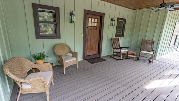 A porch with wicker chairs, a wooden door, and a ceiling fan.