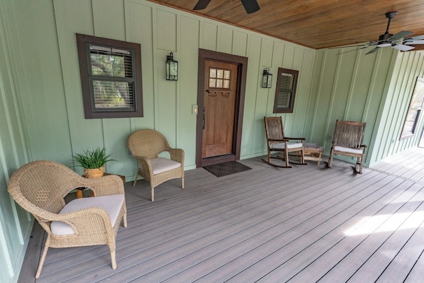 A porch with wicker chairs, a wooden door, and a ceiling fan.