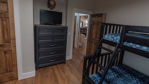 A room with a wooden dresser, a television on top, a mounted deer head, a bunk bed, and a hallway leading to another room.