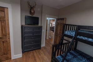 A room with a wooden dresser, a television on top, a mounted deer head, a bunk bed, and a hallway leading to another room.
