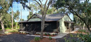 A rustic cabin with a stone foundation, wooden siding, and a gabled roof, surrounded by trees and a gravel driveway.