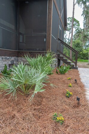 A building with a stone facade, a wooden staircase, and a landscaped area with pine straw and plants.
