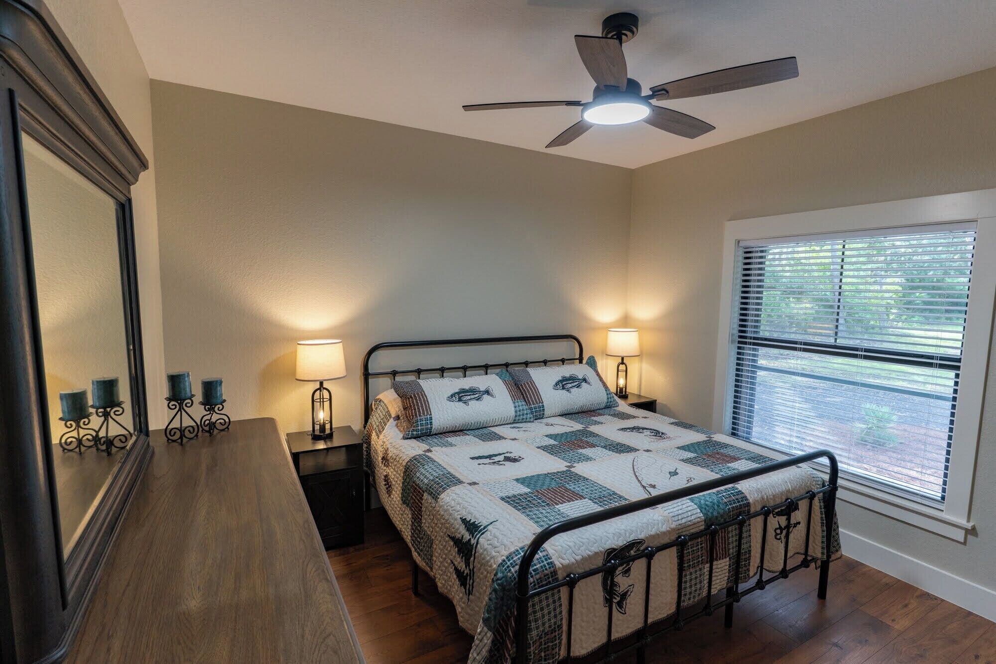 Quarto com cama, abajures, ventoinha no teto, janela com cortinas e cômoda.