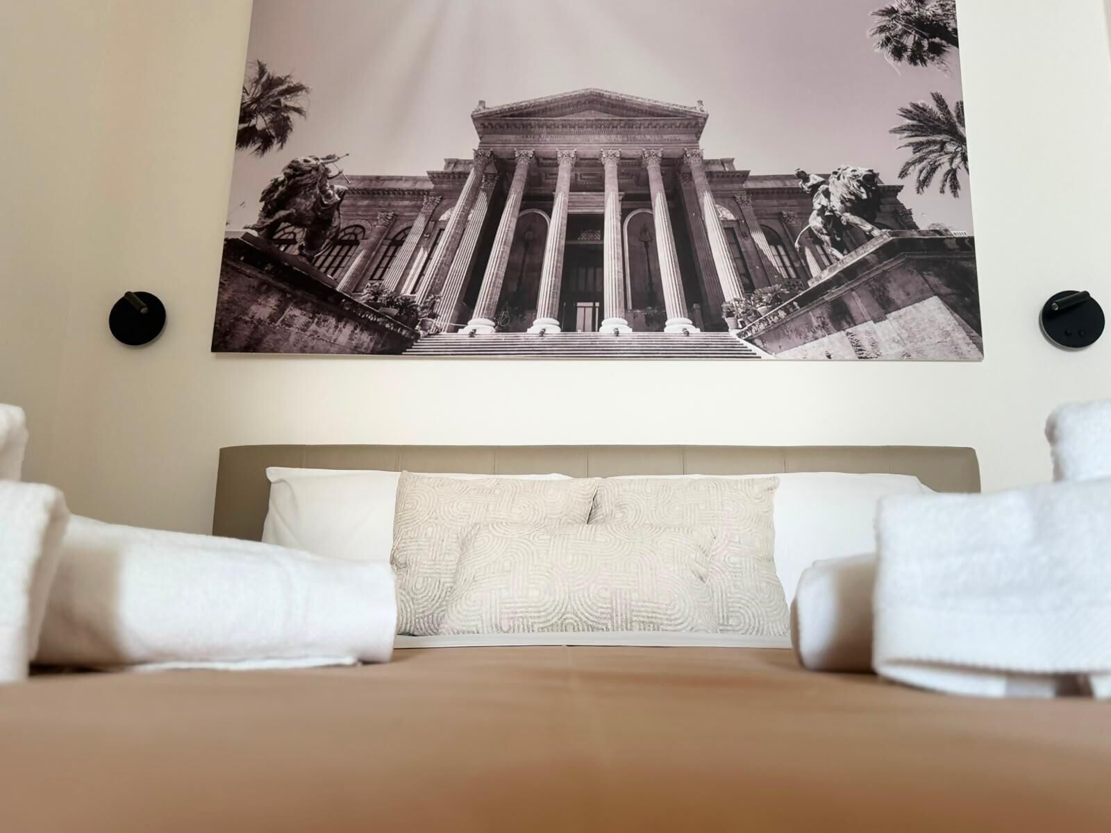 Ein Hotelzimmer mit einem großen Bett, zwei Kissen und einem Wandbild eines klassizistischen Gebäudes mit Säulen und Statuen.