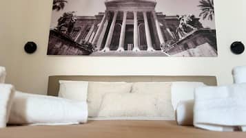 Ein Hotelzimmer mit einem großen Bett, zwei Kissen und einem Wandbild eines klassizistischen Gebäudes mit Säulen und Statuen.