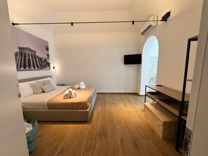 A modern bedroom with a bed, a flat-screen TV, and a wooden floor.