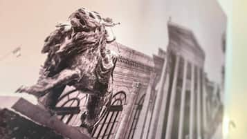 Eine Löwenstatue vor einem klassizistischen Gebäude mit Rundbogenfenstern.