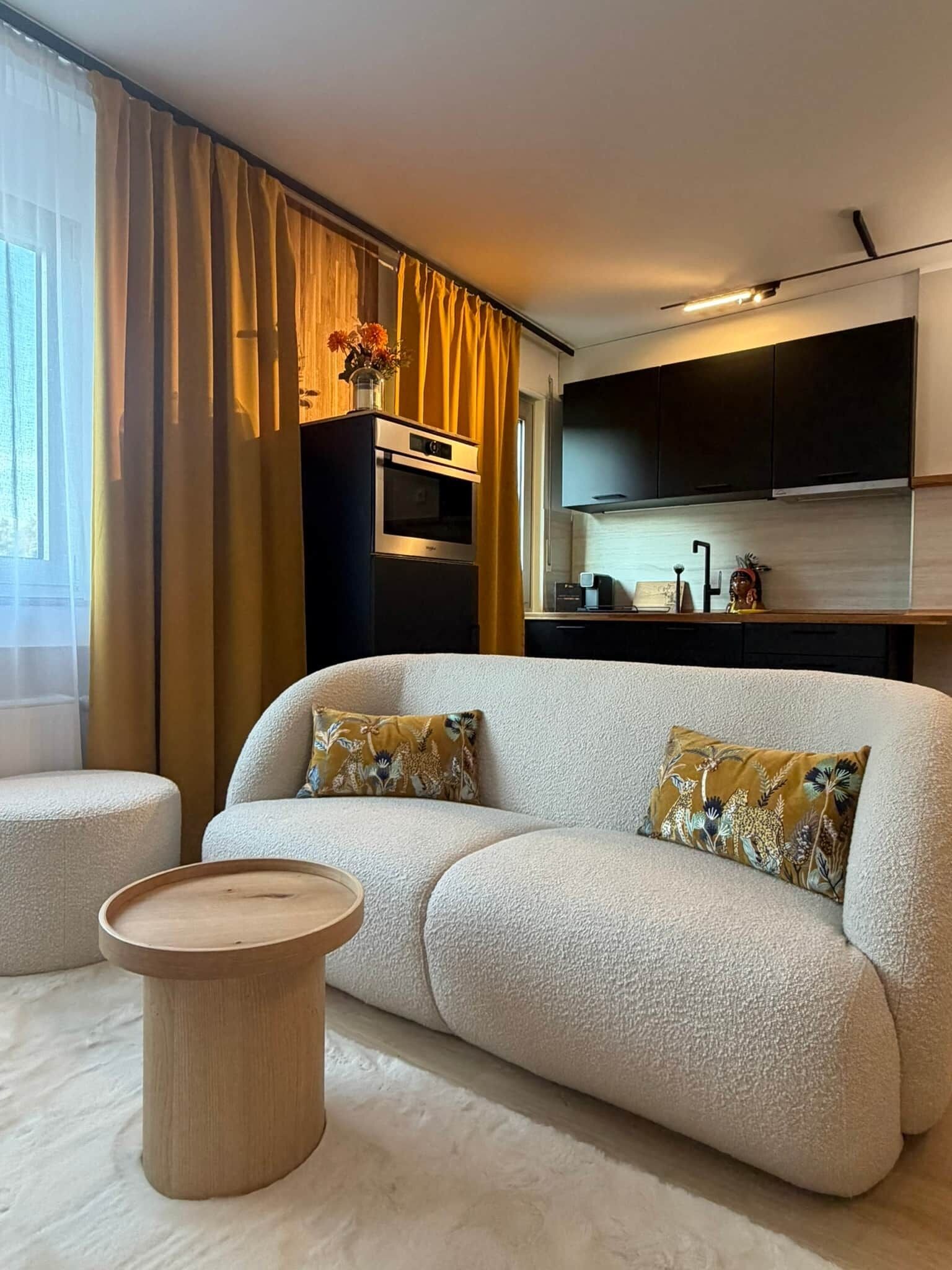 Ein modernes Wohnzimmer mit einer Couch, einem Couchtisch und einer Küchenzeile inklusive Herd und Schränken.
