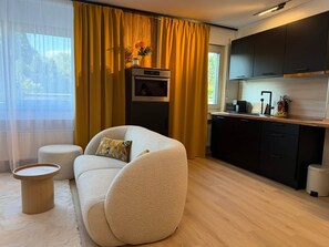 Ein modernes Wohnzimmer mit einer Couch, einem kleinen runden Tisch und einer Küchenzeile mit Kühlschrank und Schränken.