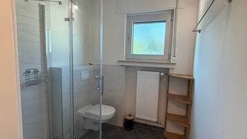 Ein modernes Badezimmer mit einer gläsernen Duschkabine, Toilette und einem Fenster über dem Waschbecken.