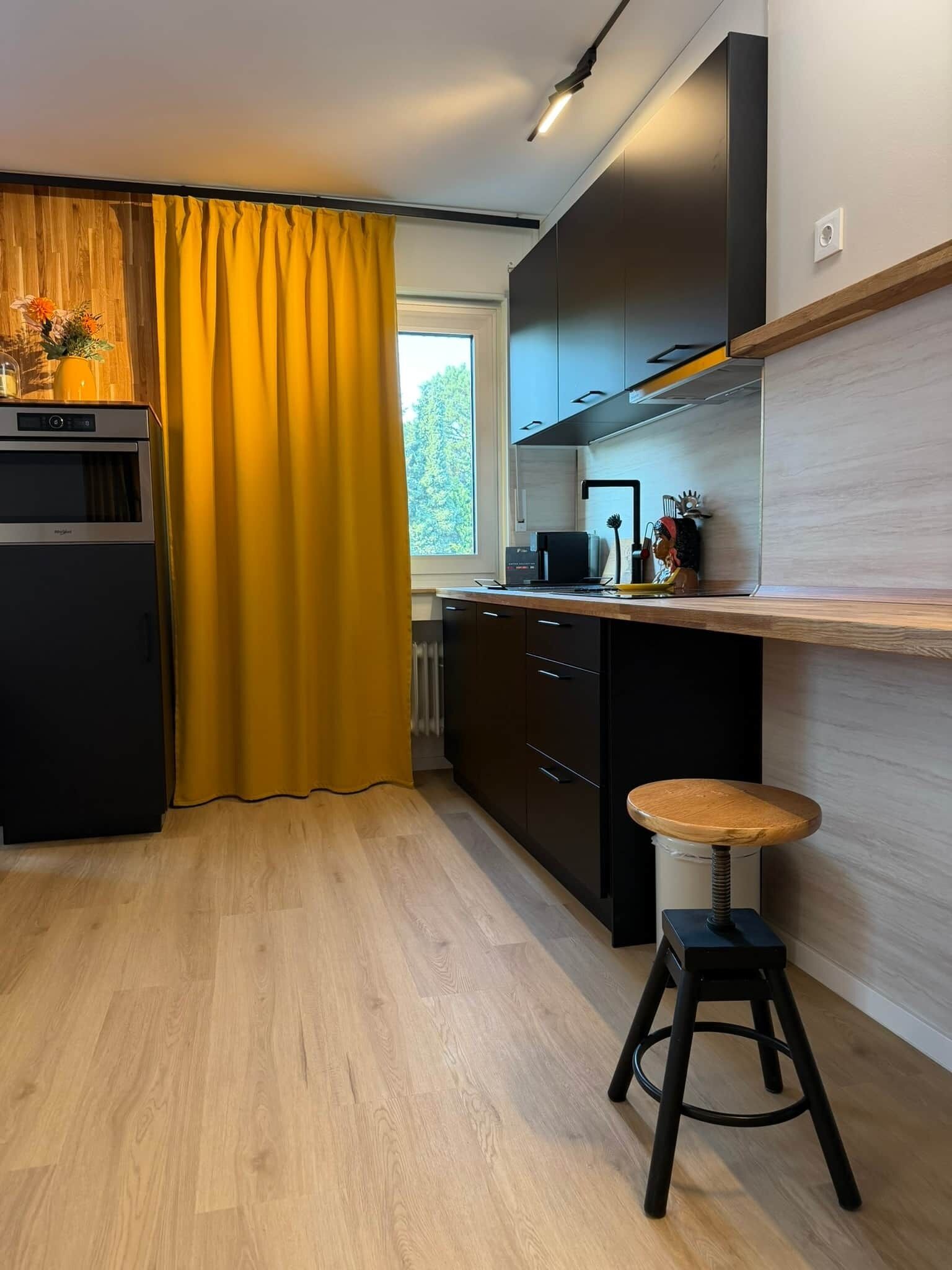 Eine moderne Küche mit einer Holz Arbeitsplatte, einem eingebauten Herd und einem Fenster mit gelben Vorhängen.