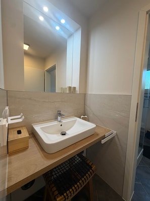 A modern bathroom with a large mirror, a white sink, and a wooden bench.
