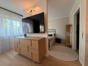 A modern bedroom with a wooden dresser, a large mirror, a bed with a headboard, and a small round rug.