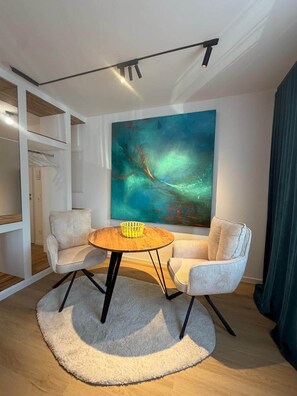 A modern living room with a round wooden table, two striped armchairs, a large abstract painting, and a ceiling track lighting system.
