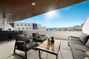 Eine Dachterrasse mit Gartenmöbeln und Blick auf die Stadtlandschaft, unter blauem Himmel.