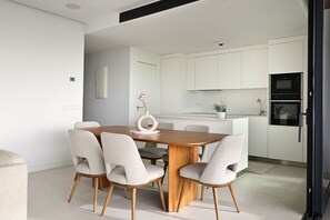 A modern kitchen with white cabinets, a built-in oven, and a dining area with a wooden table and four chairs. - Modern Apartment with Terrace in Higueron (Fuengirola)