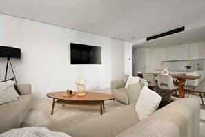 Ein modernes Wohnzimmer mit Flachbildfernseher, rundem Couchtisch und Essbereich mit Holztisch und Stühlen.