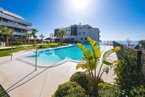 A swimming pool with a clear view of the ocean, surrounded by greenery and modern buildings. - Modern Apartment with Terrace in Higueron (Fuengirola)