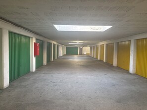 Ein langer Korridor mit grünen und gelben Türen, einem roten Notfallschrank und einem Oberlicht.