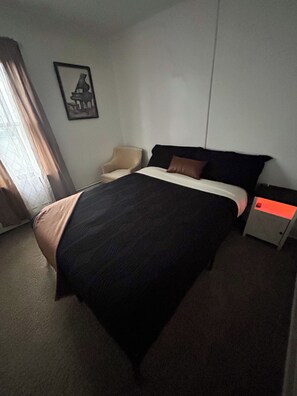 A hotel room with a bed, a chair, a nightstand, and a window with curtains.